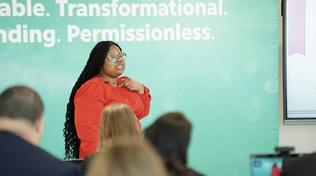 Dominque Burgess speaking on stage about scalable, transformational, permissionless education models